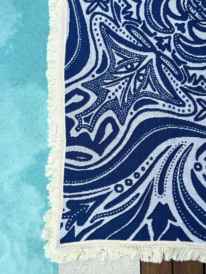 Blue Skies beach blanket or throw rug laying beside pool, showcasing the blue and white design created in Australia. 