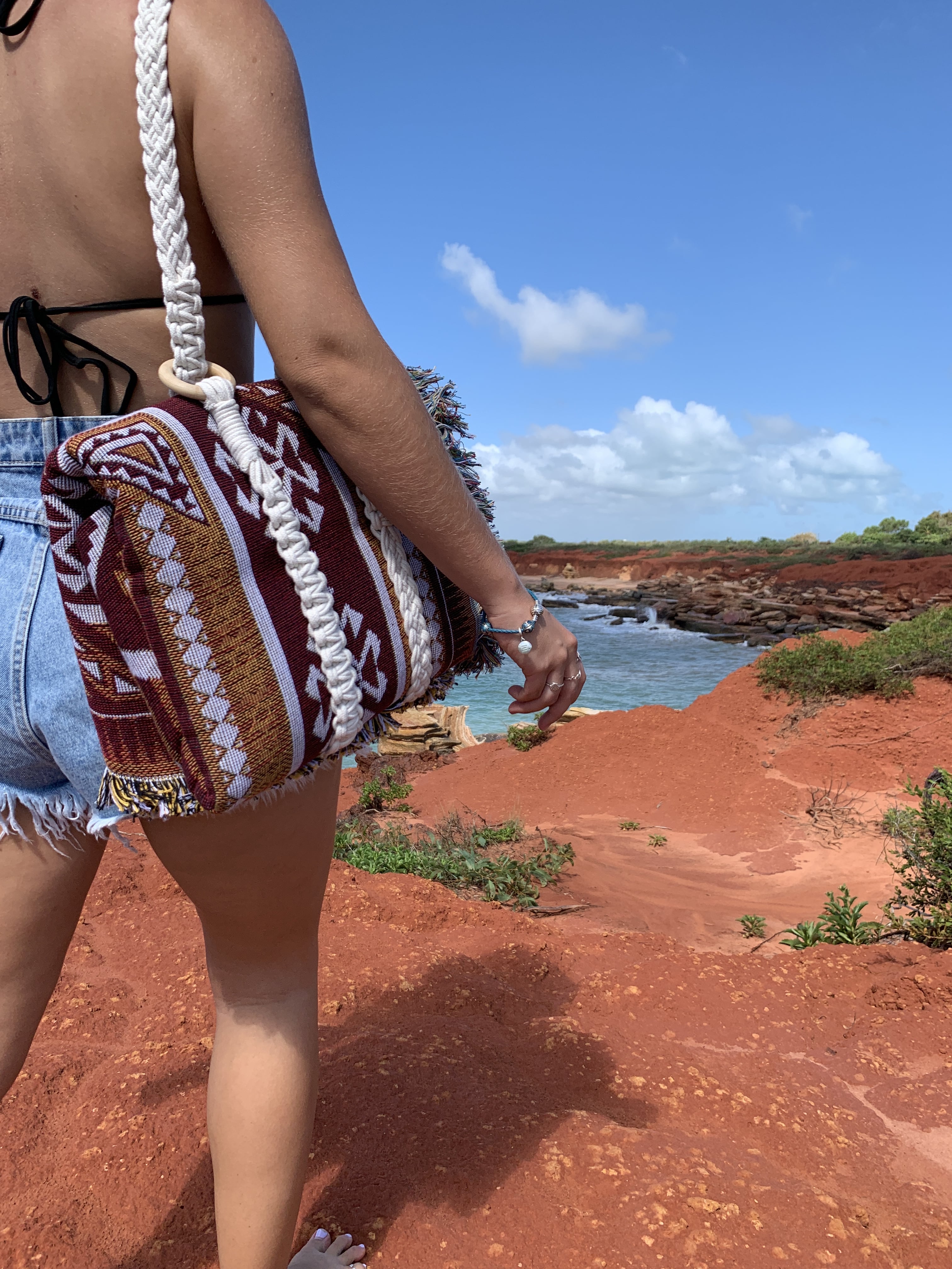 Macramé carry strap wrapped around Desert Night throw rug blanket in Western Australia red dirt overlooking ocean