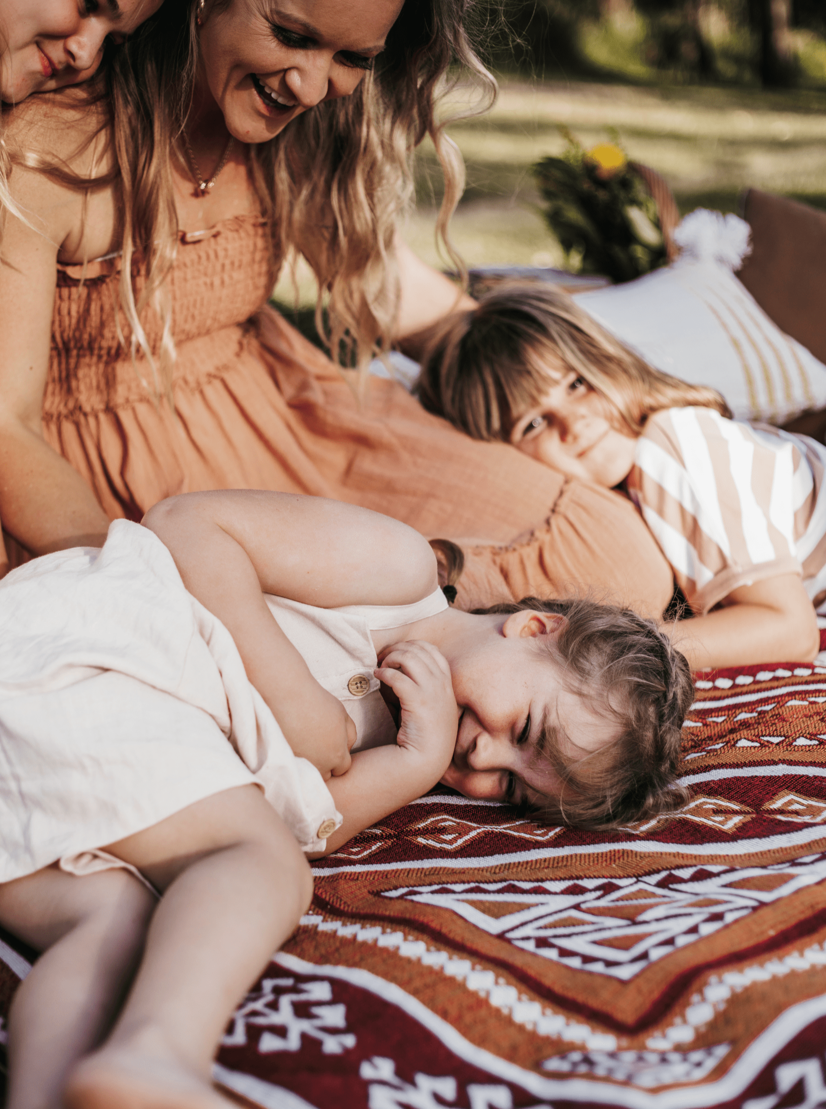 Mother with her three daughters laughing and cuddling on a Desert Night throw rug outdoors.