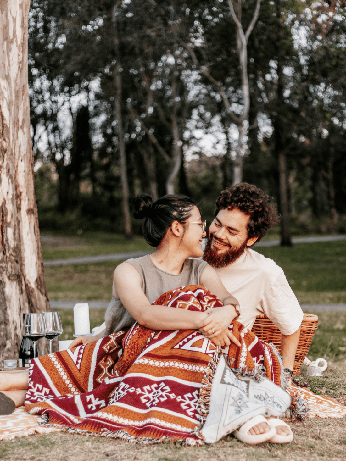 Couple cuddled up under a Desert Night throw, grazing into each others eyes. Enjoying a picnic with glasses of red wine and candles.