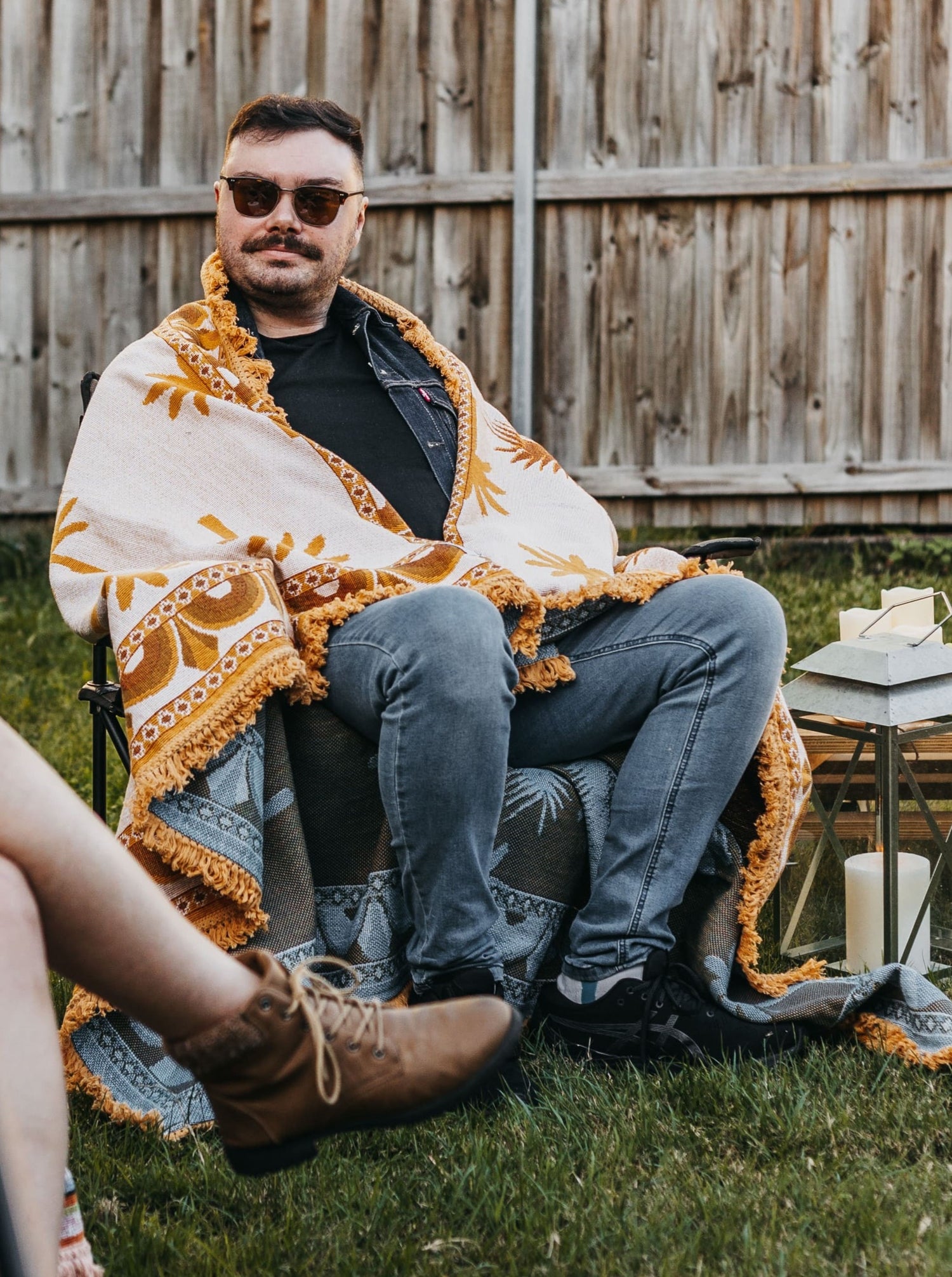 Man rugged up in Endless Summer throw blanket to keep warm while seated on camping chair in backyard party