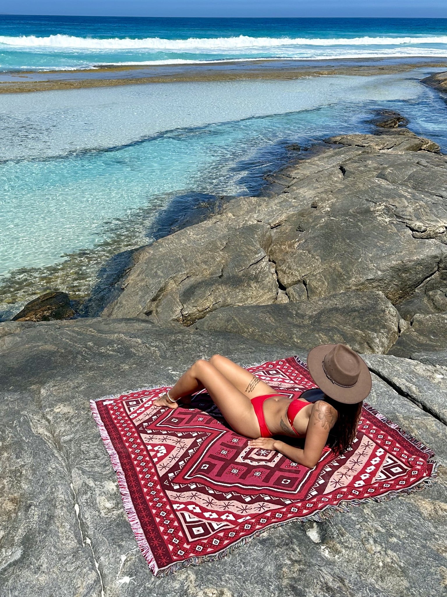 Red throw rug, beach blanket on rocks overlooking crystal blue water in Western Australia.