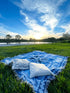 Shooting Stars blue throw rug, picnic blanket laying on grass overlooking sunset. Designed in Aus.