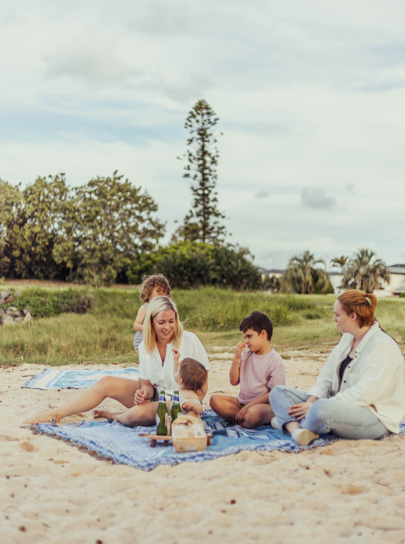 Shooting Stars blue throw rug, picnic blanket laying on beach in Brisbane as family plays and has a picnic. Designed in Aus.